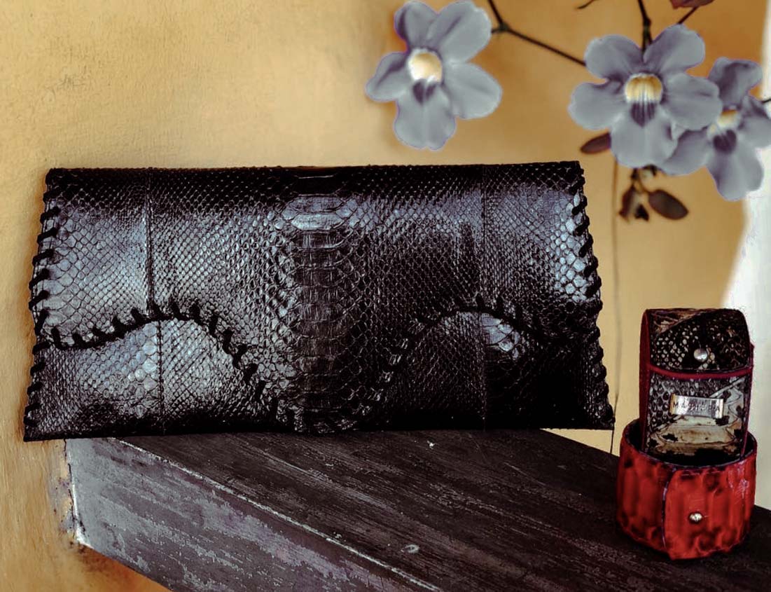 Clutch INGA en piel de pitón negro, sobre textura de madera y pulseras ÁMBAR en piel exótica de Mashera.