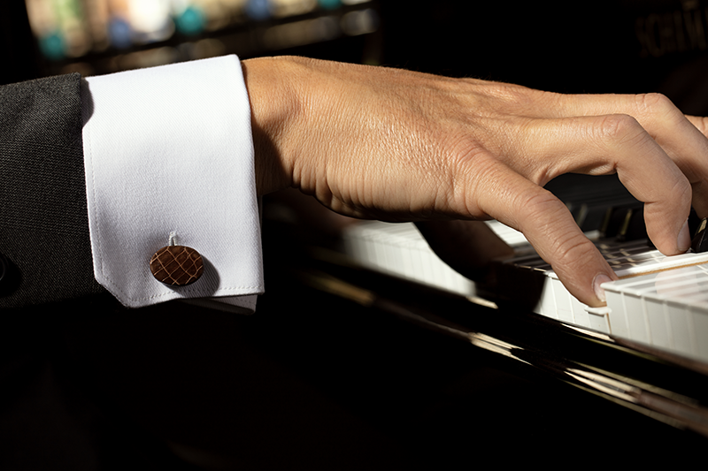 Modelo al piano luciendo gemelos WOMO en piel de pitón - exotismo sofisticado para un look formal.
